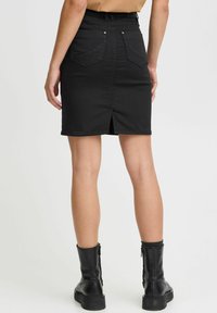 Black denim skirt with a back slit, two rear pockets, and a mid-rise waist. The fabric is smooth with a slight stretch. Worn with black ankle boots.