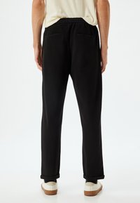 Sorte sweatpants med elastisk talje, to baglommer og opbukkede manchetter. Båret med hvide sko med brune såler.