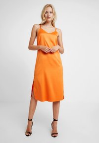 Orange ärmlös klänning med rak skärning, sidospjäll och mjuk textur. Stylad med svarta remklackar.