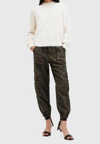 Weißer, flauschiger Pullover mit überschnittenen Schultern, kombiniert mit dunkelgrünen Leopardenmuster-Cargo-Hosen mit elastischen Bündchen. Schwarze, hochhackige Sandalen.