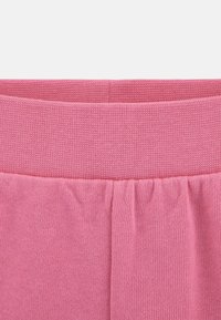 Ceinture en tricot rose avec un motif texturé, présentant de légères fronces le long du bord inférieur. Material doux et extensible, idéal pour le confort.