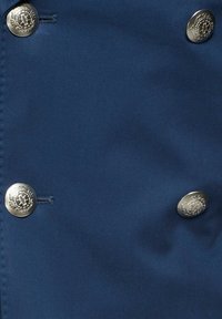 Granatowa tkanina o gładkiej fakturze, zdobiona trzema dekoracyjnymi srebrnymi guzikami z misternymi wzorami. Brak widocznych szwów ani dodatkowych detali.