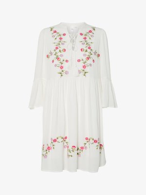 Vestido blanco con mangas largas y acampanadas, decorado con bordados florales en rosa y púrpura. Los flecos decorativos y la cintura fruncida añaden textura.