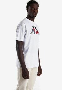 Camiseta de algod�ón blanca con un diseño gráfico colorido de dos figuras en jeans rojos y azules. Con mangas cortas y estilo de cuello redondo.