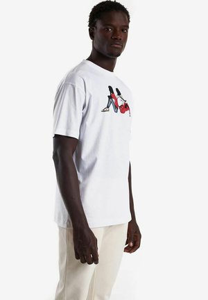 Camiseta de algodón blanca con un diseño gráfico colorido de dos figuras en jeans rojos y azules. Con mangas cortas y estilo de cuello redondo.