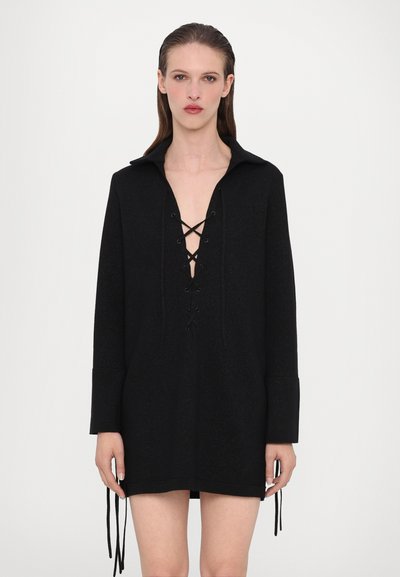 Robe pull noire avec un décolleté en V profond, un devant à lacets, des manches longues et des liens sur les côtés. Fabriquée dans un tissu texturé avec une coupe décontractée.