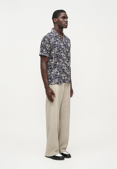 Tmavomodrá košeľa s krátkym rukávom a bielym kvetinovým vzorom; kombinovaná s ľahkými béžovými širokými nohavicami a čiernymi topánkami s bielymi akcentmi.