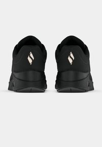 Čierne atletické topánky s textúrovanou gumovou podrážkou, hladkým zvrškom a nenápadným logom na zadnej strane. Obsahujú polstrovaný golier pre pohodlie.