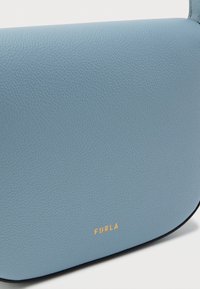 Világoskék bőrválltáska texturált felülettel, lekerekített formájú, arany "Furla" logóval és kontrasztos fekete szegéllyel.