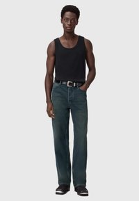 Canottiera nera, jeans blu scuro a gamba dritta e taglio rilassato, cinta nera e scarpe nere con accenti argentati.