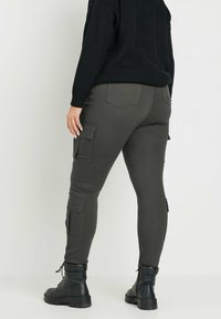 Pantalones cargo verde oscuro con dos bolsillos laterales, un diseño ajustado y una textura suave, combinados con botas negras de cordones.