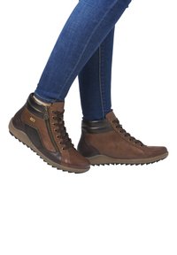 Baskets montantes marron avec une tige en cuir texturé, des accents noirs, des détails en zip doré et une semelle en caoutchouc avec un motif de traction.