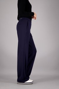 Marineblaue weit geschnittene Hose aus glattem Stoff, mit vorderem Falten, Seitentaschen und einem dezenten Taillenschild. Getragen mit weißen Sneakern.