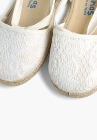 Valged espadrillid, mis on varustatud tekstureeritud pitsilised disainid, juute taldadega ja elastsete rihmadega, tagamaks kindlat istuvust. Lamedad kujundid ümmarguste varvastega.