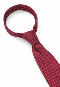 Red tie with a textured pattern of small white dots. Smooth fabric, narrow design, and a classic knotted style at the neck.