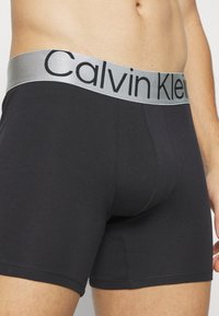 Black cotton boxer briefs featuring a soft silver waistband with "Calvin Klein" branding, fitted design, and smooth texture.