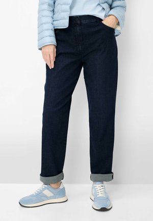 Persona che indossa jeans blu scuro con risvolto, sneakers azzurro chiaro con dettagli bianchi, una giacca imbottita azzurro chiaro e una maglia azzurro chiaro.