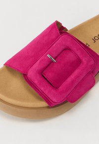 Fuchsia mockaskinnsläpsandaler med en bred rem med en stor fyrkantig spänne och en tan färgad plattformsula. Slät textur, minimal hårdvara.