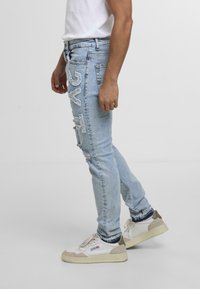 Heledsinine denim-tekstuuriga teksad, millel on kulunud aktsendid ja istuv disain. Kombineeritud beežide ja valgete tossudega, luues mugava ilme.