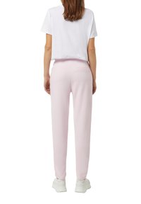 Rosa Sweatpants aus weichem Stoff, mit schmaler Passform, elastischem Bund und einer Rückentasche, kombiniert mit einem weißen, kurzen T-Shirt.