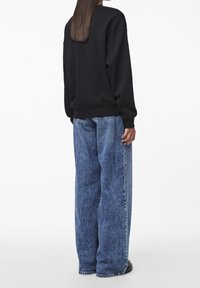 Černá oversized mikina s žebrovanými manžetami a lemem, spárovaná se světle modrými širokými džíny s vybledlou texturou a surovými lemy.