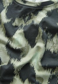 Detailní záběr na pomačkanou látku s abstraktním černobéžovým vzorem a viditelným stehem podél okraje.