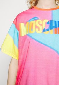 Camiseta de manga corta colorida con un vibrante degradado de rosa, amarillo y azul, con la palabra "MOSCHINO" en letras audaces y multicolores.