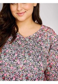 Czarny kwiatowy top z małymi różowymi, żółtymi i białymi kwiatami, z dekoltem w szpic i miękką, teksturowaną tkaniną. Luźny krój, krótkie rękawy.