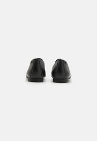 Bailarinas de cuero negro con textura suave, punta redondeada, tacón bajo y detalles de costura sutiles en la parte trasera. Diseño minimalista.