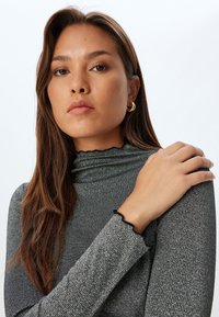 Grauer, metallischer Rollkragenpullover mit strukturiertem Finish und schwarzen Rüschenärmeln. Glattes Material und enganliegendes Design.