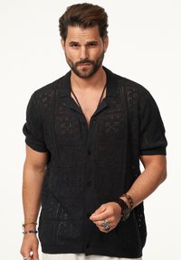 Schwarzes gehäkeltes Shirt mit kurzen Ärmeln und Kentkragen, das ein kunstvolles Lochmuster und gerippte Bündchen aufweist.