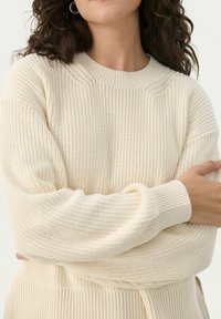 Crème-kleurige gebreide trui met een gestructureerde weefsel, geribbelde manchetten en een ronde hals. Heeft een relaxte pasvorm en gedetailleerde stiksels.