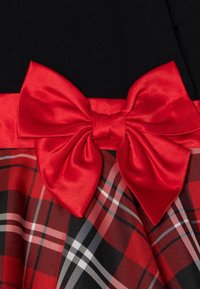 Rode satijnen strik bevestigd aan een zwart en rood geruit stof met een effen zwarte achtergrond.