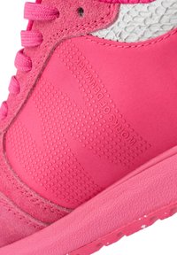 Rosa Sporteschuh mit einer strukturierten Wildleder- und glatten Synthetik-Oberfläche, prominenten Perforationen und kontrastierenden gemusterten Akzenten.