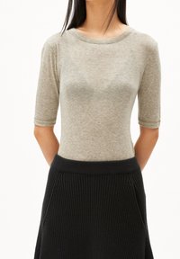 Světle šedý top s krátkým rukávem a kulatým výstřihem, vyrobený z měkké látky, v kombinaci s černou žebrovanou sukní s bočními kapsami.