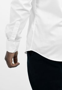 Witte lange mouwen shirt met knoopmanchetten en op maat gemaakte zoom, gecombineerd met donkere broeken. Heeft een gladde textuur en een strak design.