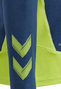 Niebieska koszulka sportowa z teksturowanym zielonym panelem bocznym oraz dwoma zielonymi paskami chevron na rękawie, podkreślająca dynamiczne elementy designu.