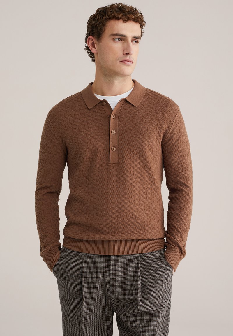 Polo à manches longues marron texturé avec col et patte à trois boutons, associé à un pantalon taille haute à carreaux.