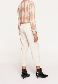 Beige och vit argyle-tröja, krämfärgade kordbyxor med uppvikta fållar, och svarta anklarboots med spetsig tå. Texturerade tygdetaljer synliga.