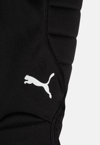 Svarta träningsleggings med en texturerad design, kontrasterande vit Puma-logga och subtila sömdetaljer längs sömmen.