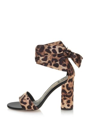 Sandały na wysokim obcasie w panterkę z szerokim paskiem wokół kostki, detalem w formie węzła oraz solidną czarną podeszwą. Teksturowany materiał i design na słupkowym obcasie.