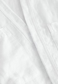 Gros plan sur un tissu blanc texturé avec des coutures visibles et deux poches rectangulaires de chaque côté.