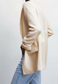 Beige blazer med en afslappet pasform, lange ærmer, to sidelommer og en glat tekstur, parret med lyseblå denim jeans.