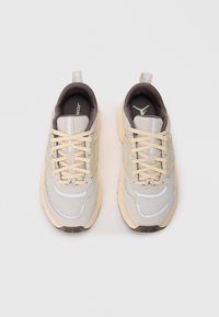 Para beżowych i żółtych sportowych sneakersów z siateczkowego materiału, sznurowadłami oraz logo na języku i wkładce, widziana z góry na białym tle.