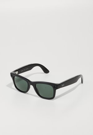 Sorte plastiksunglasses med grønne linser, rektangulær form, med et sølvlogo på armen og et robust rammedesign.