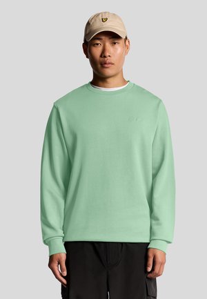 Mintgrøn langærmet sweatshirt med ribbede manchetter, broderet logo, lagdelt over en hvid t-shirt; båret med en beige baseball cap.
