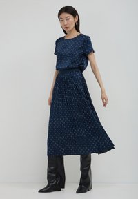 Abito blu navy con pois bianchi, maniche corte, gonna plissettata e vita elastica, abbinato a stivali neri al ginocchio.