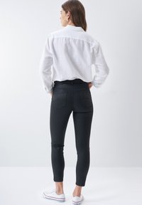 Jeans negros ajustados con una cintura alta, combinados con una camisa blanca de botones de corte holgado. Presenta bolsillos traseros sutiles y un diseño de largo por el tobillo.