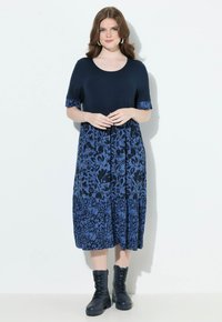 Granatowa sukienka w kwiaty z krótkimi rękawami, o wielowarstwowym kroju. Połączona z czarnymi, sznurowanymi botkami. Materiał wydaje się miękki i lekki.