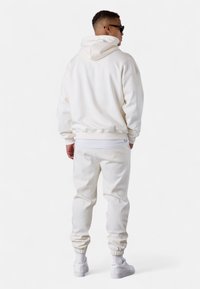 Weiße Kapuzenjacke und Jogginghosen aus weichem Stoff, mit lockerer Passform. Rippbündchen an den Ärmeln und am Bund, die das Outfit mit Sneakers abrunden.